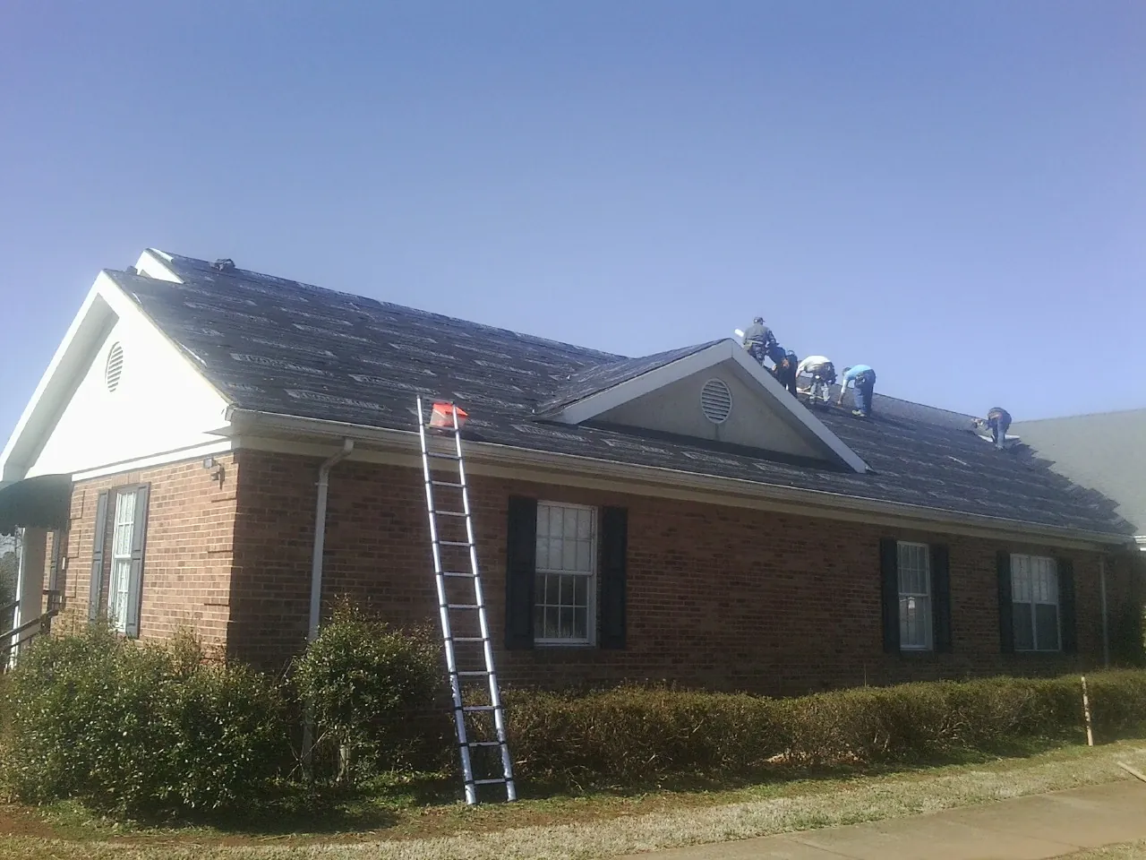 Crew tearing shingles off a brick ranch roof with a ladder set — Metal Roof Repair work by our crew in Dassel