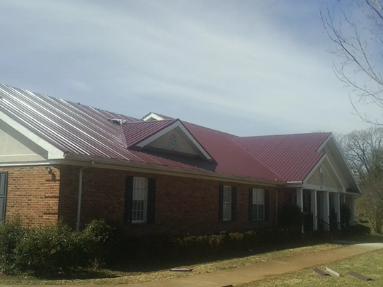 Red metal roof with gabled entries on a long brick building, from a Hail Damage Roof Repair job in Dassel