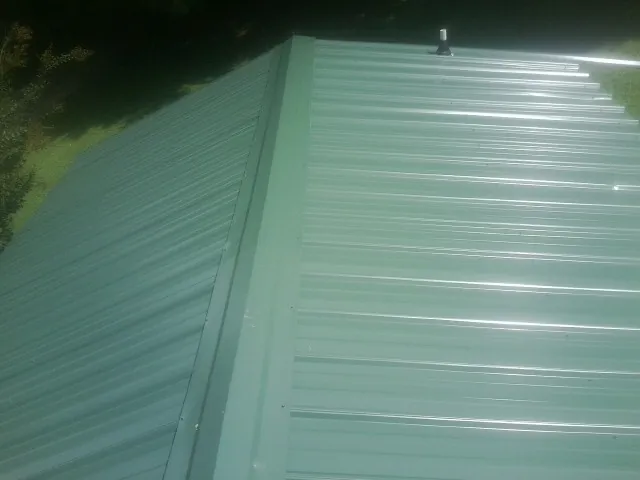 New green metal panels meeting at the ridge of a roof — Flat Roof Repair work by our crew in Dassel