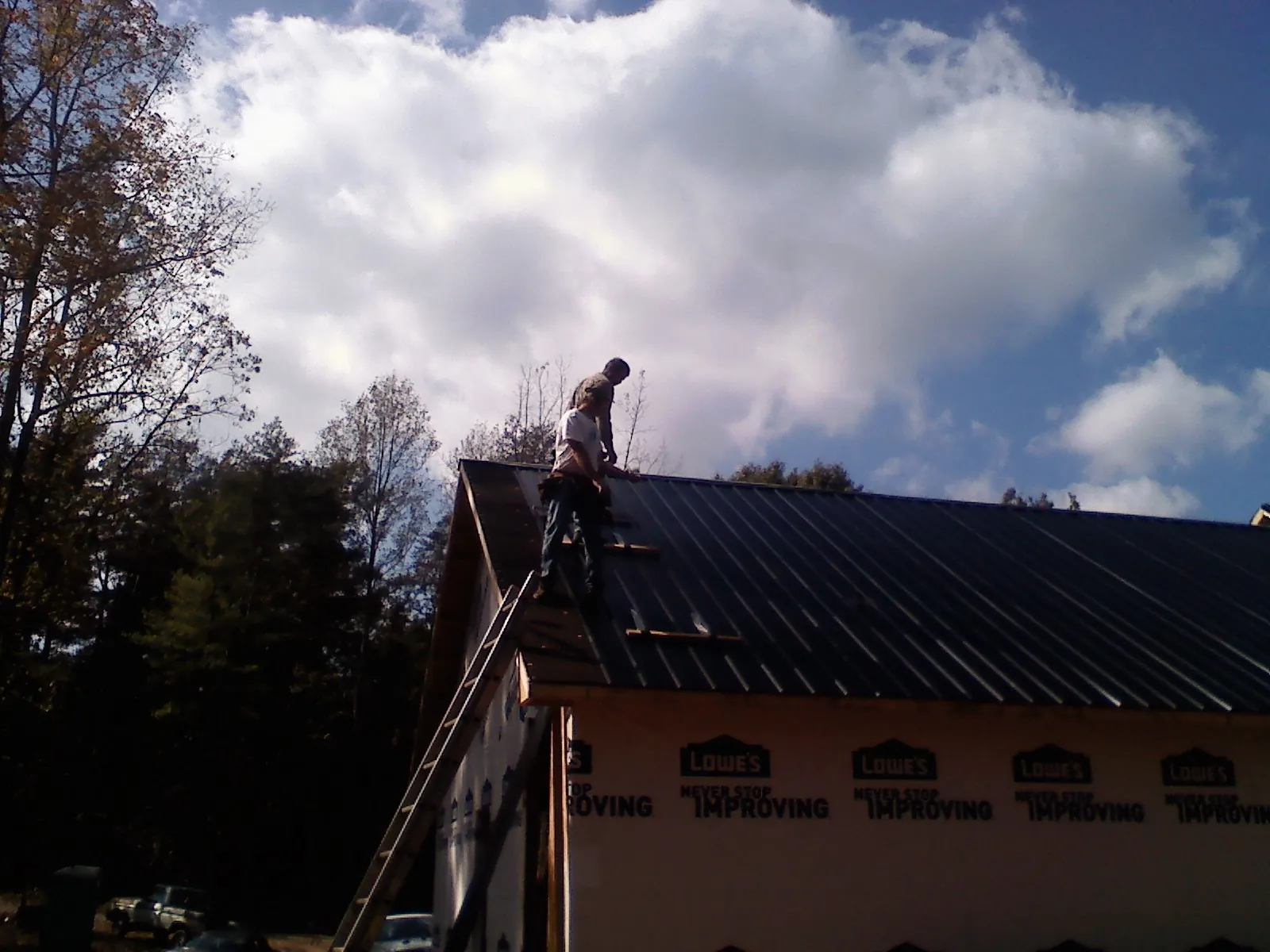 Roofer fastening dark metal panels high against a cloudy sky, from a Roof Inspection job in Dassel
